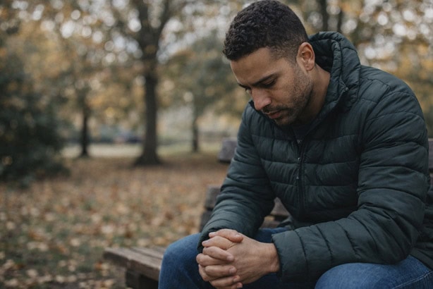 man sitting with head bowed on a park bench - stress and anxiety